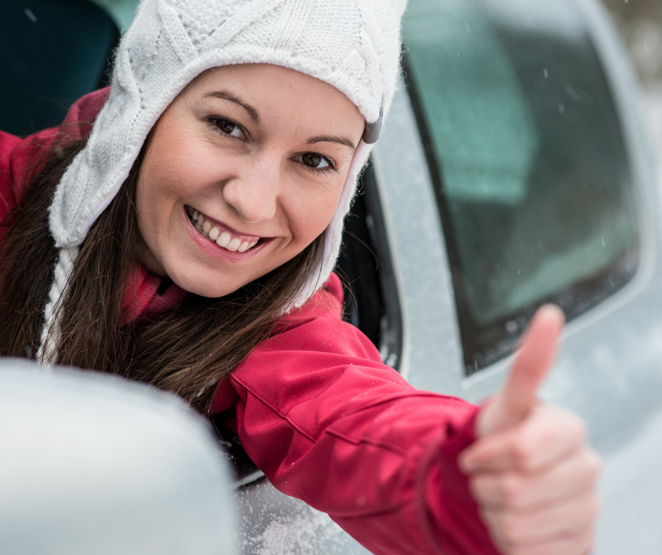 girl with white hat and red coat leaning out car window, smiling with thumbs up