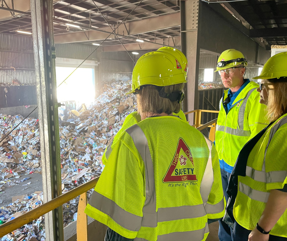 people in yellow neon yellow vests and hard hats looking at pile of trash
